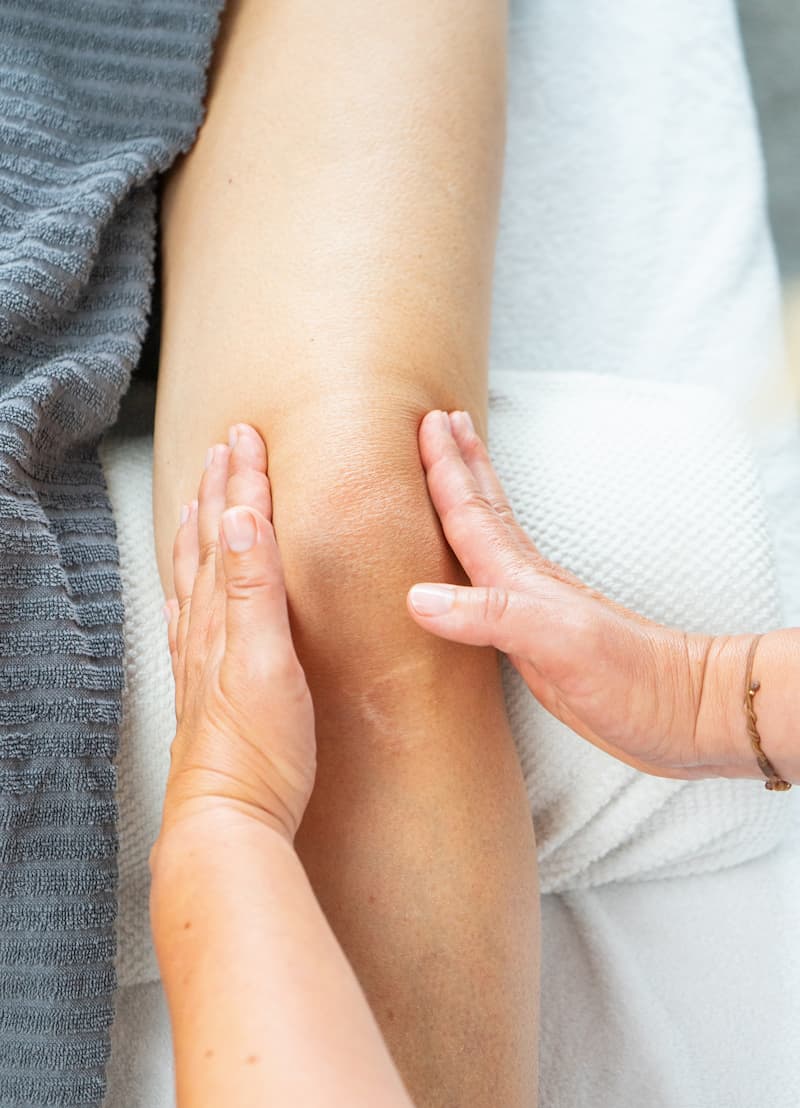 Zwei Hände massieren den Bereich rund um das Knie.